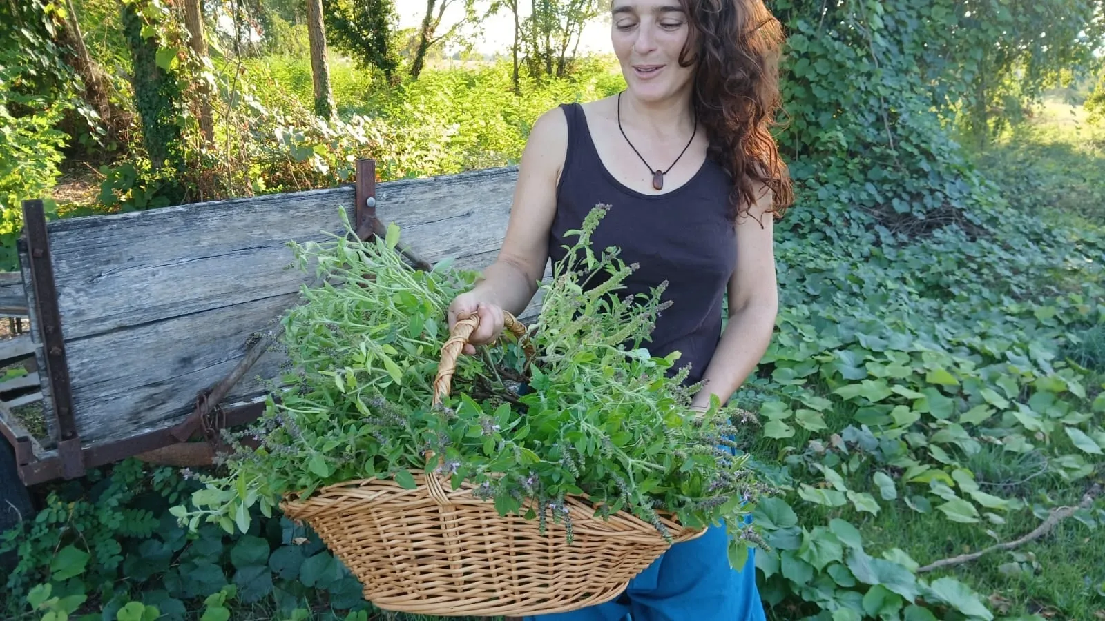 Cécile Anselmino au jardin, tenant un panier d’osier rempli de plantes fraîchement cueillies